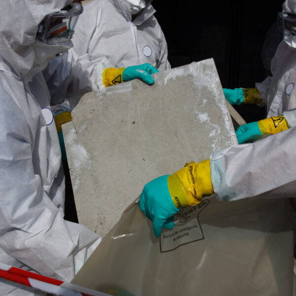 Workers wearing protective suits and gloves placing asbestos materials into sealed disposal bags.