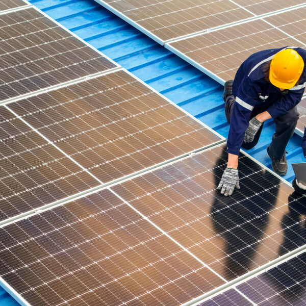 Two engineers in safety helmets inspecting solar panels on a roof with a laptop.