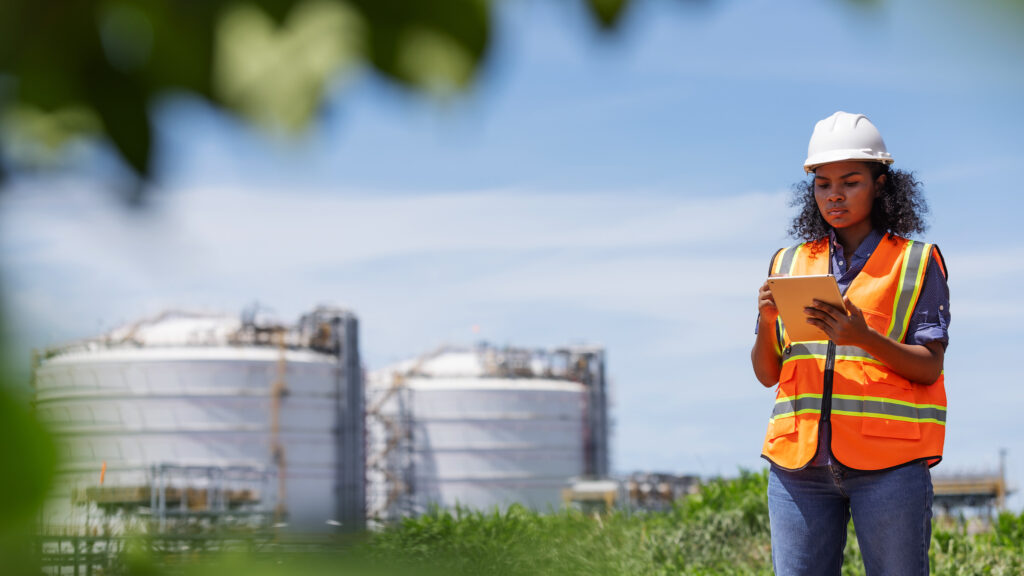 Person wearing safety gear and a high-visibility vest using a tablet during an environmental site inspection.