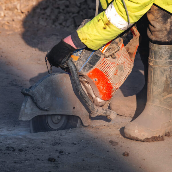 Person cutting concrete with a handheld power saw, creating dust and vibration.