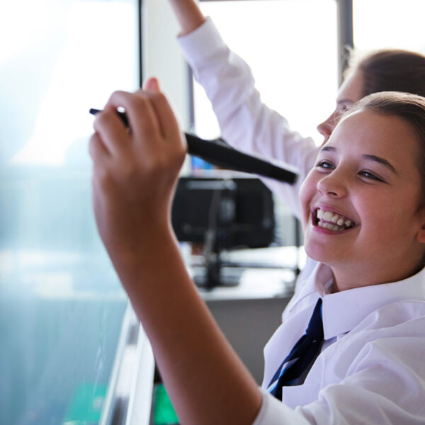 Smiling student writing on a classroom whiteboard.