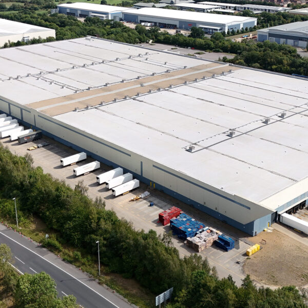 Aerial view of a large logistics warehouse with loading bays and lorries parked outside.